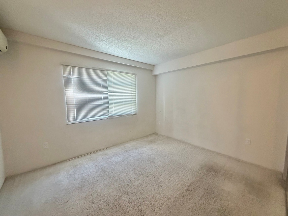 A room with a carpeted floor and a window with blinds.